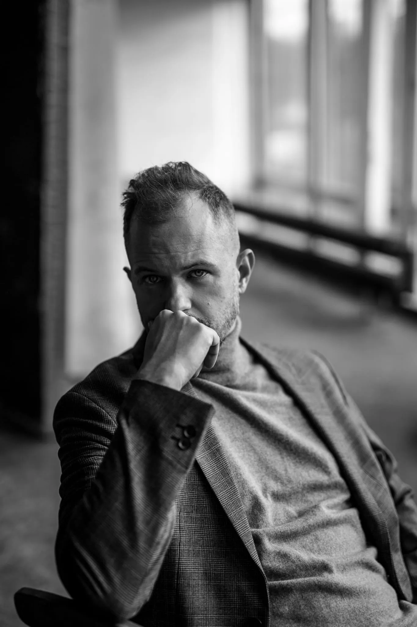 Tomasz Żółtak siedzi w jasnym, architektonicznym wnętrzu, dłoń przy ustach, zamyślone spojrzenie
