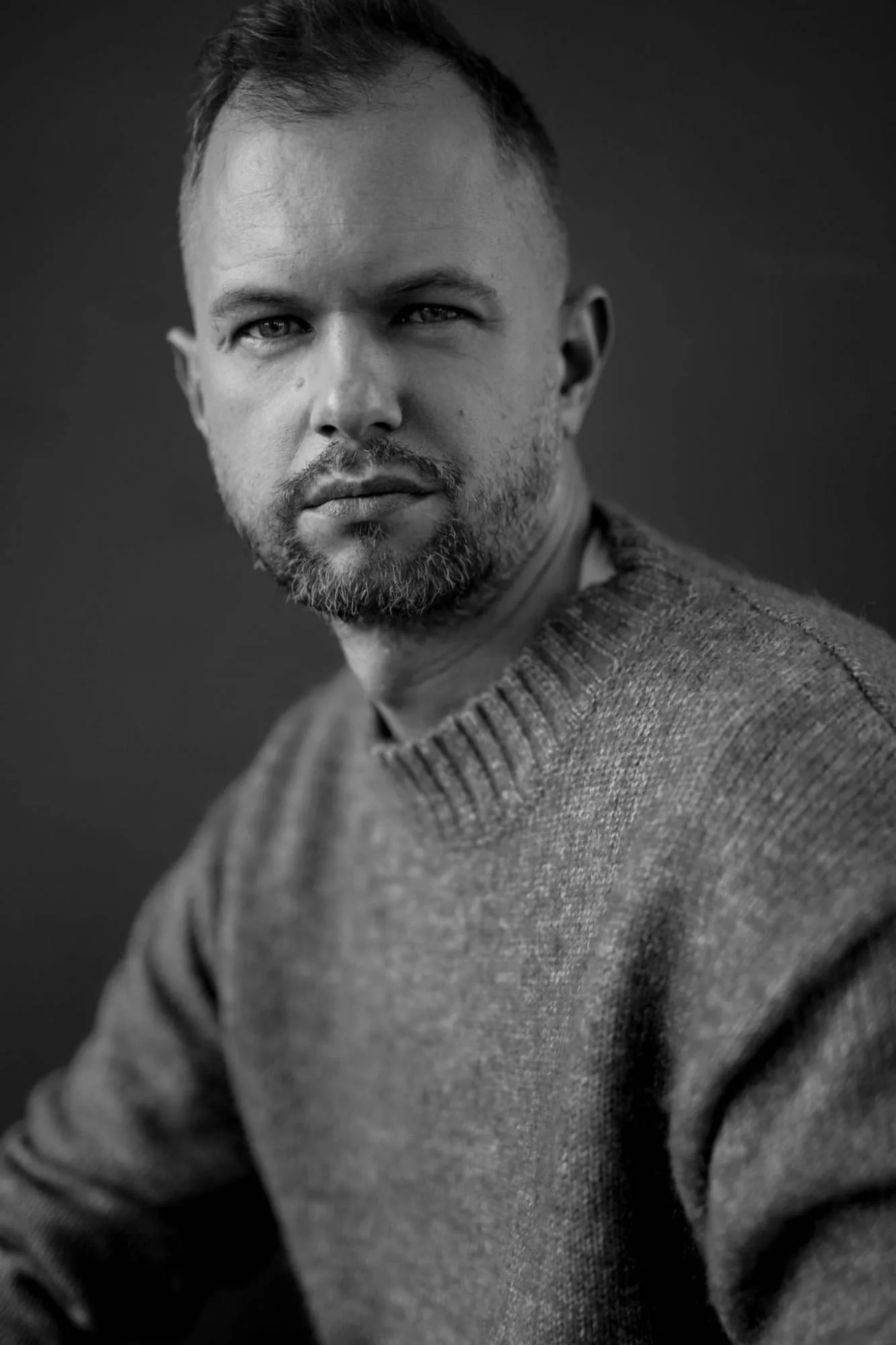 Tomasz Żółtak na ciemnym tle, w szarym swetrze, spojrzenie skierowane w obiektyw